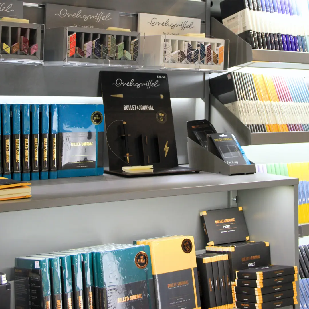 Leuchtturm1917 Bullet Journal Display. Shelf with Bullet Journal versions of notebooks and Drehgriffel, standard versions in the background.
