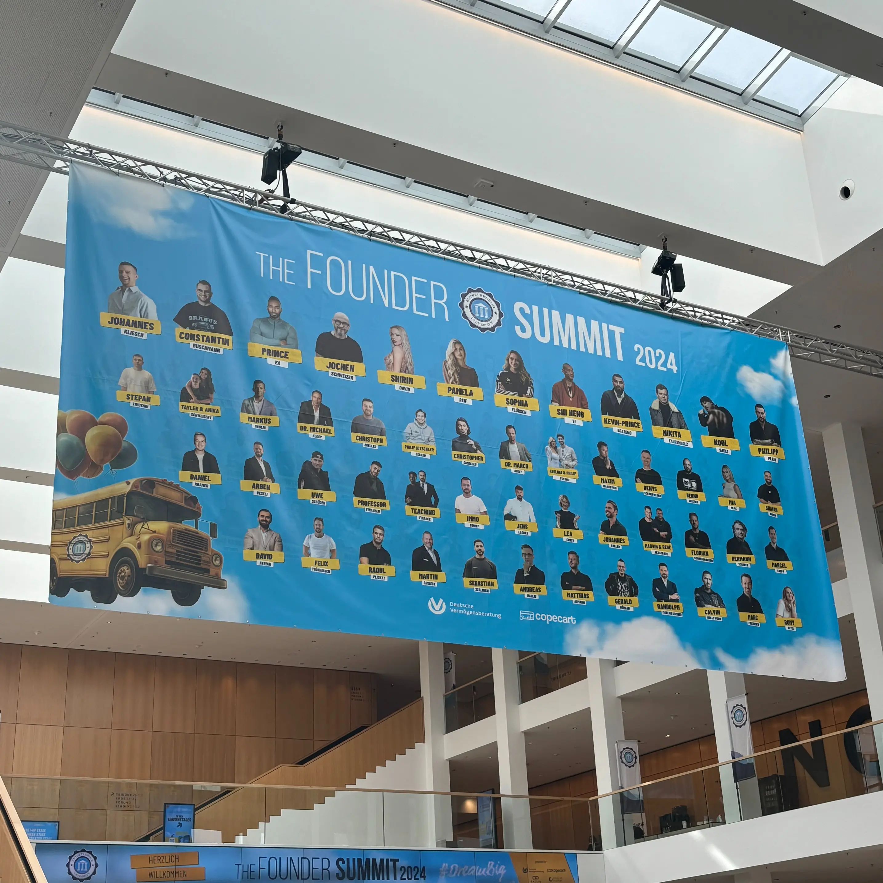 Veranstaltungsbanner Founder Summit 2024. Large banner with portraits and text “The Founder Summit 2024” in event hall.