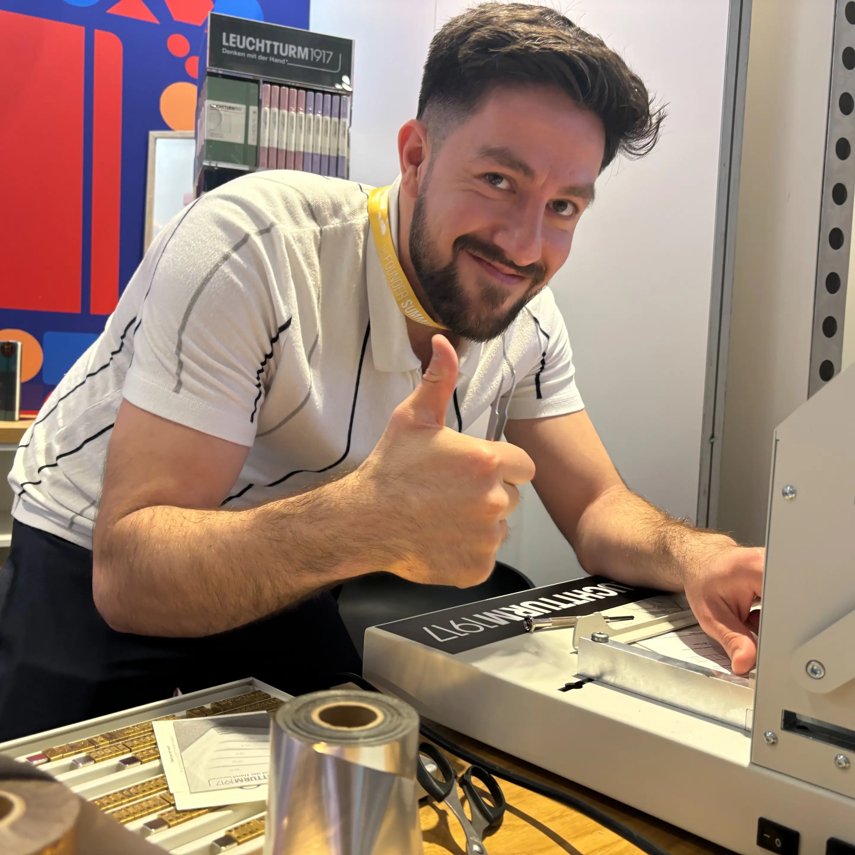 Leuchtturm1917 Liveprägestation auf dem Founder Summit 2024. Man at embossing station giving thumbs up, LEUCHTTURM1917 stand in background.