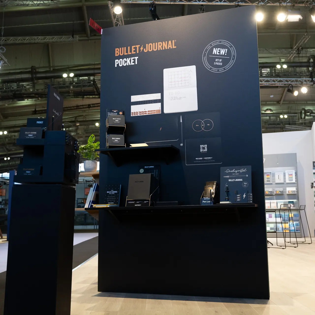 Messedisplay von LEUCHTTURM1917 auf der Ambiente 2024 mit Produkten aus der Bullet Journal Pocket Serie auf einer dunklen Präsentationswand.
