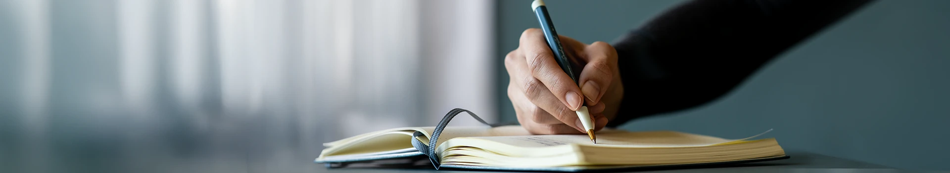 Leuchtturm1917 Writers and Thinkers Banner. Eine Hand schreibt mit Kugelschreiber in ein Notizbuch.