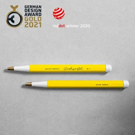 Zwei gelbe Drehgriffel Nr. 1 mit goldfarbener Spitze und eingraviertem Beispielnamen, daneben die Auszeichnungen „German Design Award Gold 2021“ und „Red Dot Winner 2020“, präsentiert auf grauem Hintergrund.