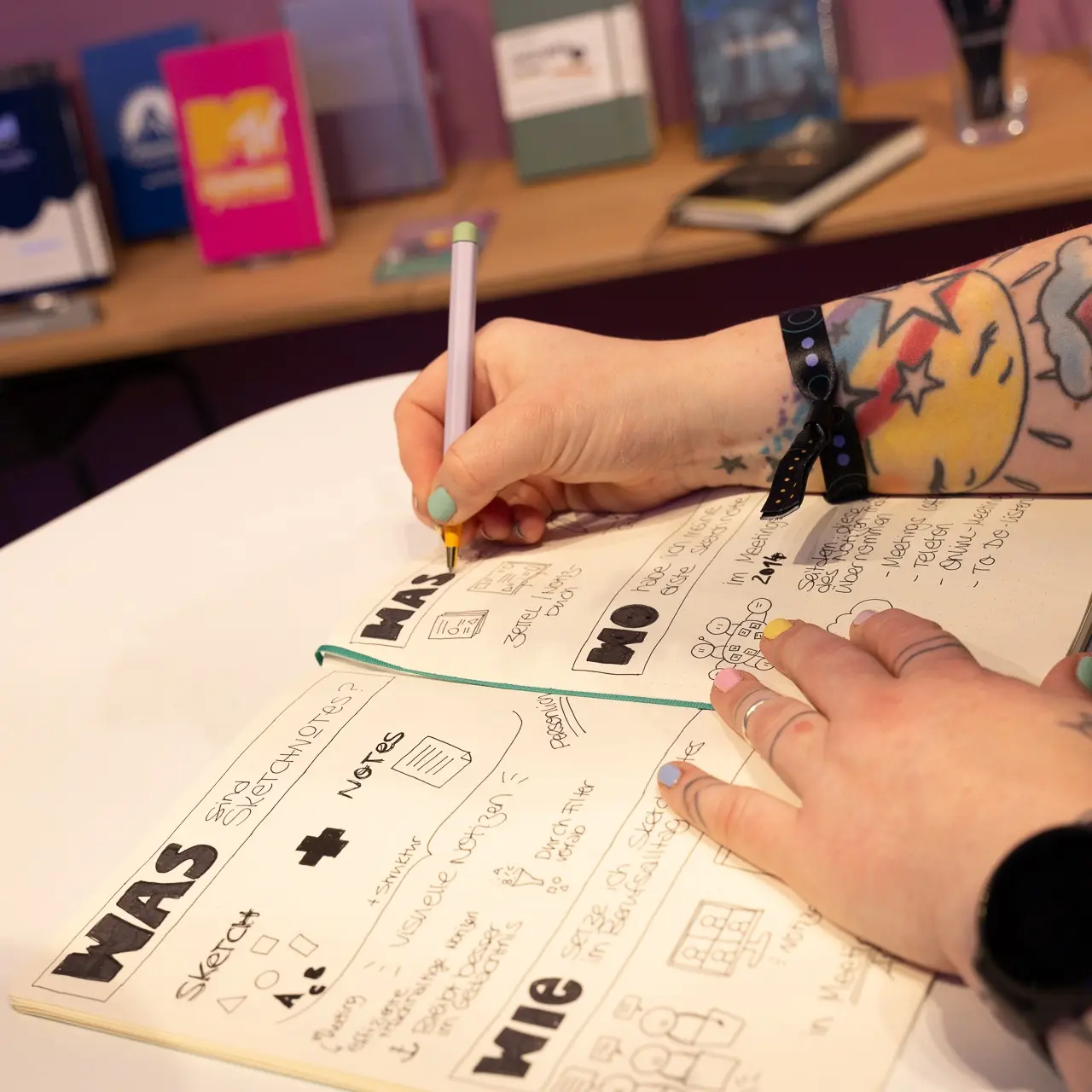 Detailaufnahme OMR2025. Person writes with a pen in an open notebook with sketches and text.