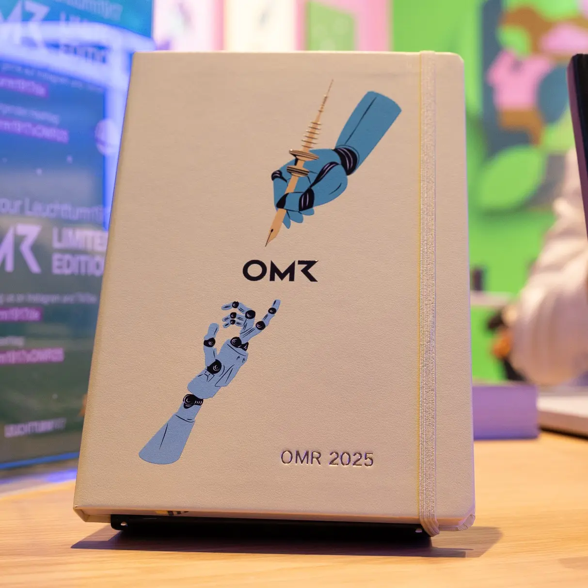 OMR notebook with illustration of two hands and embossing “OMR 2025”.