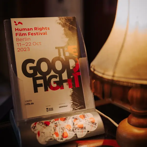Program booklet in a display stand, title “THE GOOD FIGHT”, table lamp beside it.