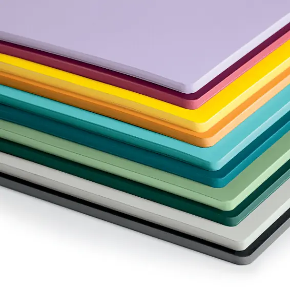 Das Jottbook Double Farbsortiment. Stacked notebooks in lilac, burgundy, yellow, orange, turquoise, green, grey and black, pages match covers.