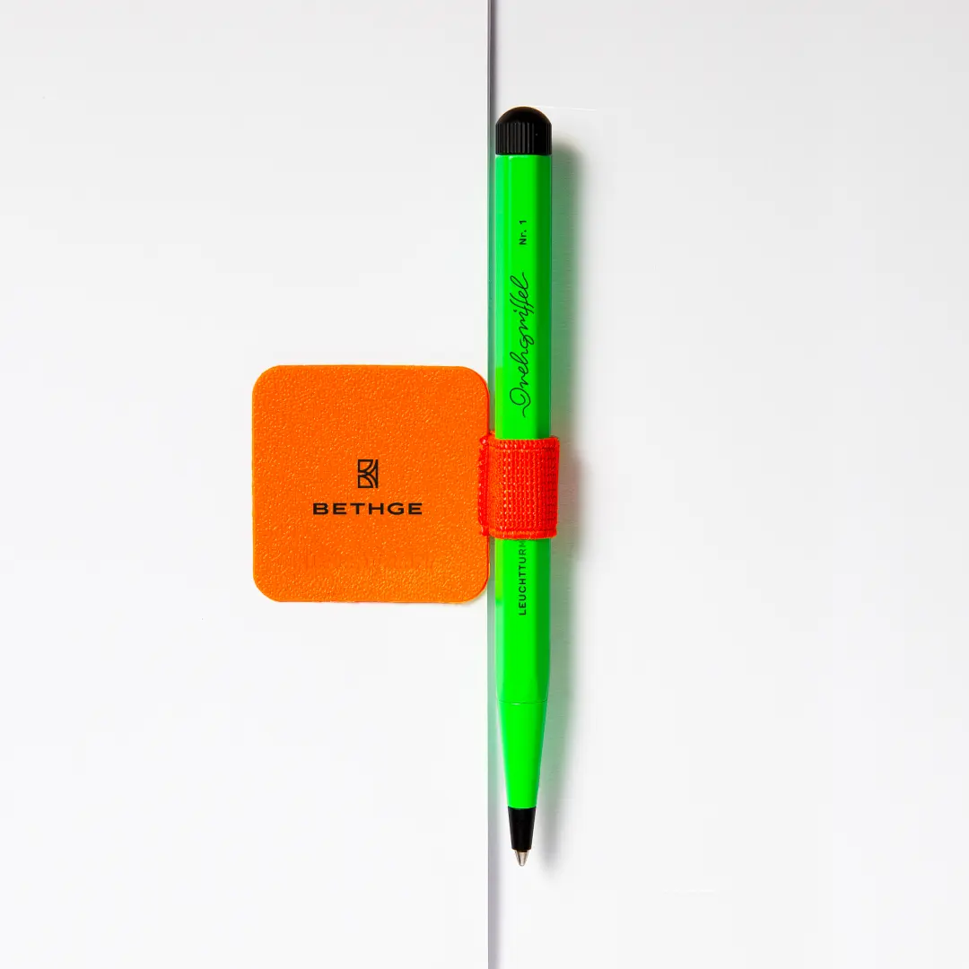Leuchtturm1917 Luminous Edition Penn Neon green Drehgriffel with neon orange pen holder, next to a square element with “BETHGE”.