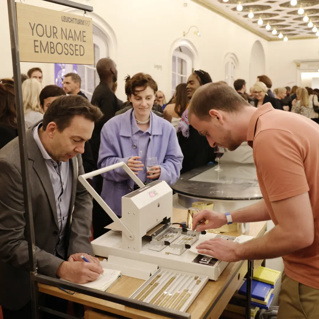 Trade fair stand with embossing station, visitors emboss notebooks, sign “Your Name Embossed”.