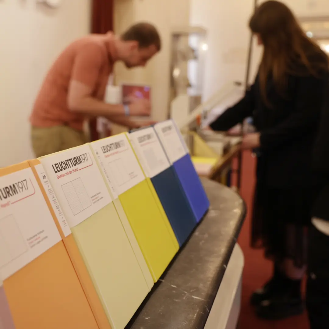 First Steps Award – Leuchtturm1917 Notizbücher Row of colorful LEUCHTTURM1917 notebooks on counter, embossing station in background.