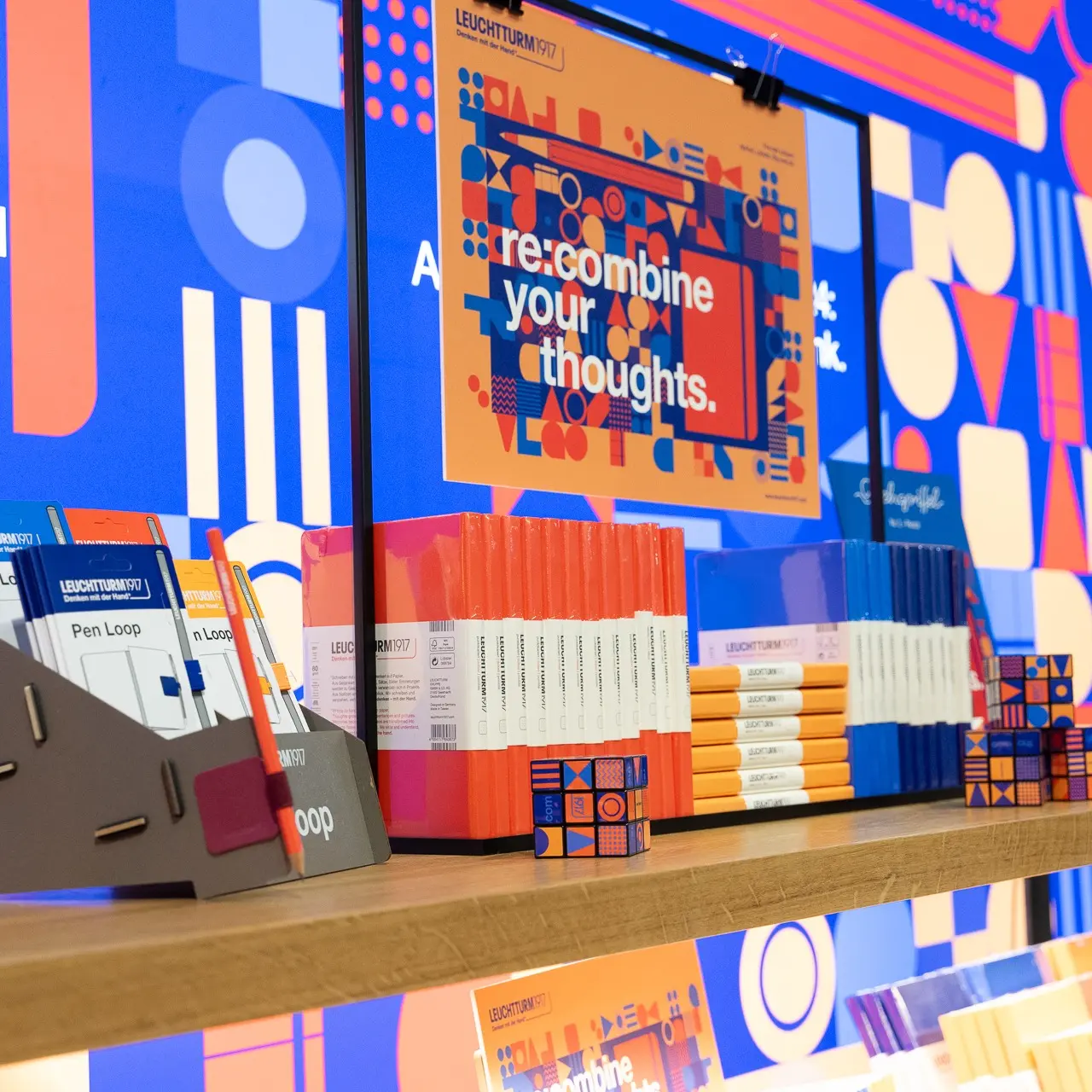 Bunte Leuchtturm1917-Produktpräsentation. LEUCHTTURM1917 display with notebooks, Pen Loop, Rubik’s-style cube and “re-combine your thoughts.”.
