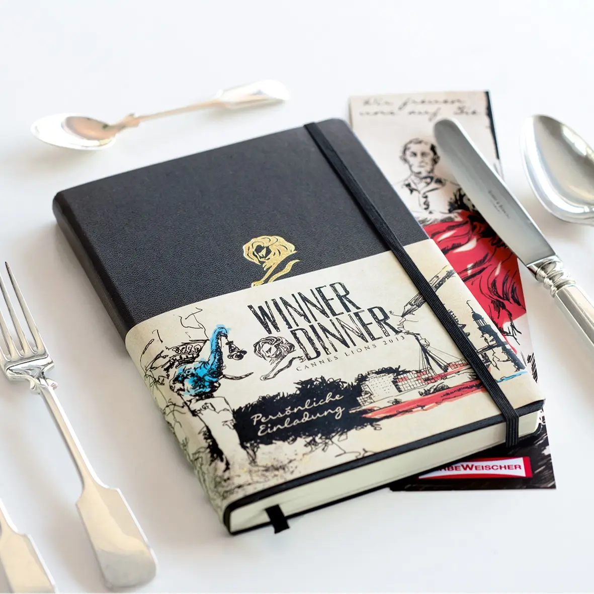Black notebook with band “WINNER DINNER Cannes Lions 2013” and cutlery.