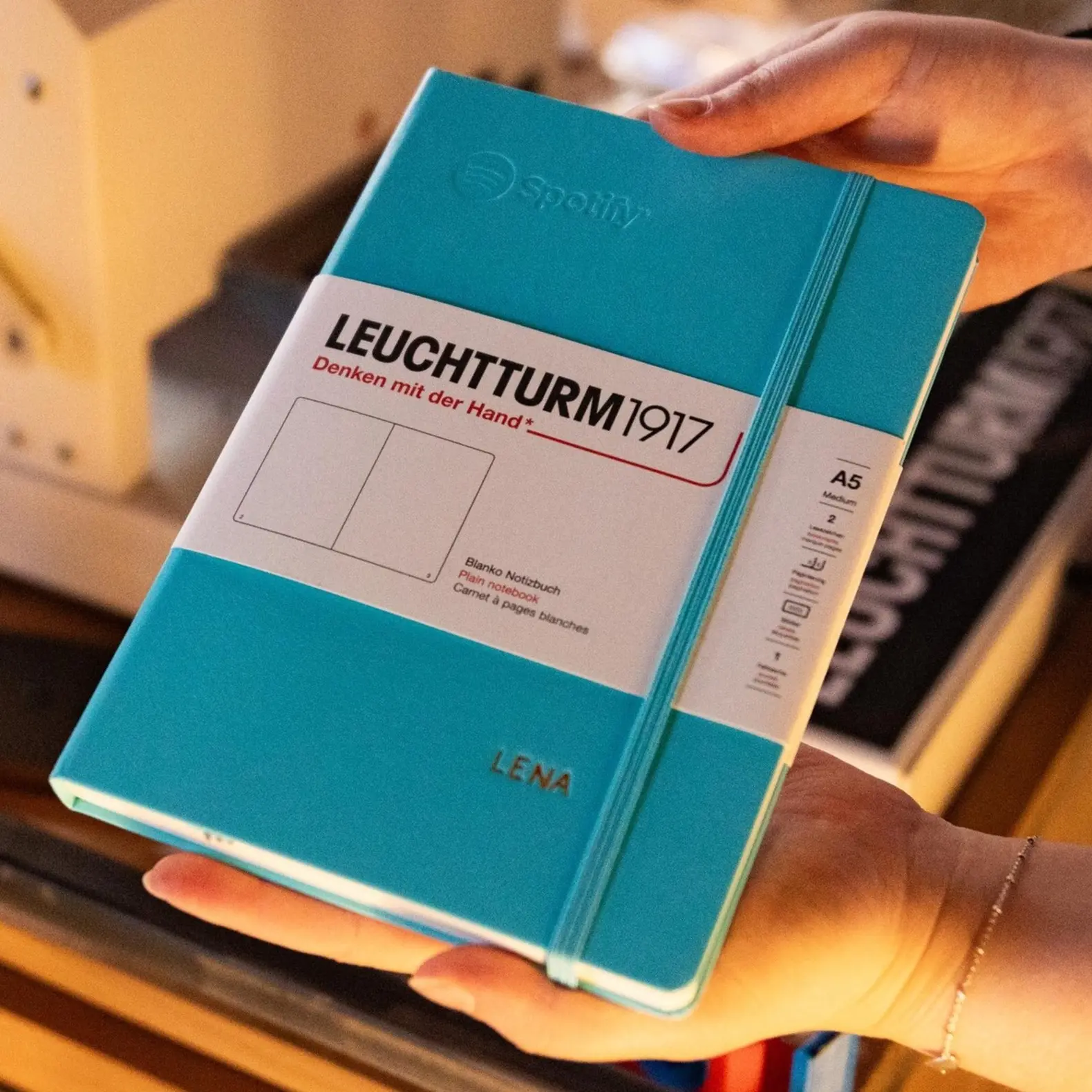 Spotify All Ears x Leuchtturm1917 Live-Prägeevent. Close-up of a turquoise LEUCHTTURM1917 A5 notebook with embossing “LENA”.