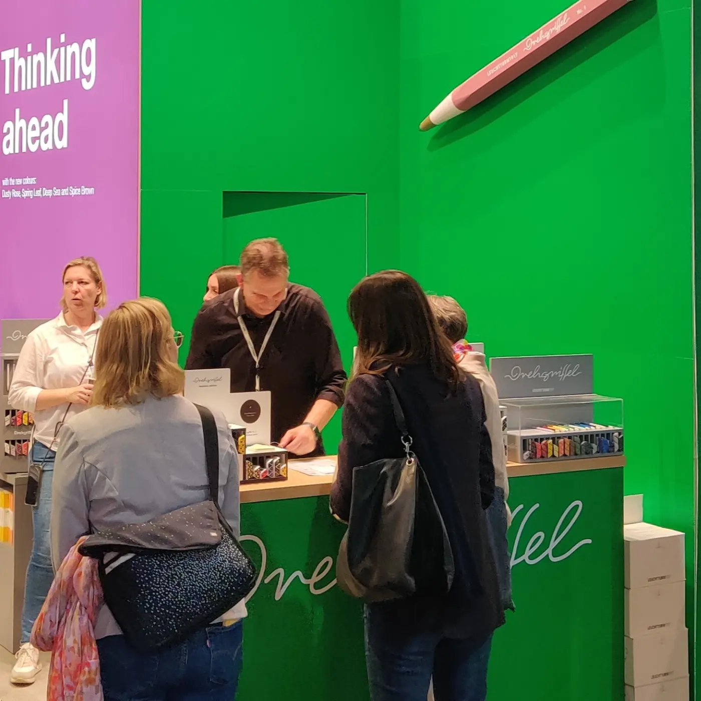 Staff advise visitors at the Drehgriffel stand in front of a green wall.