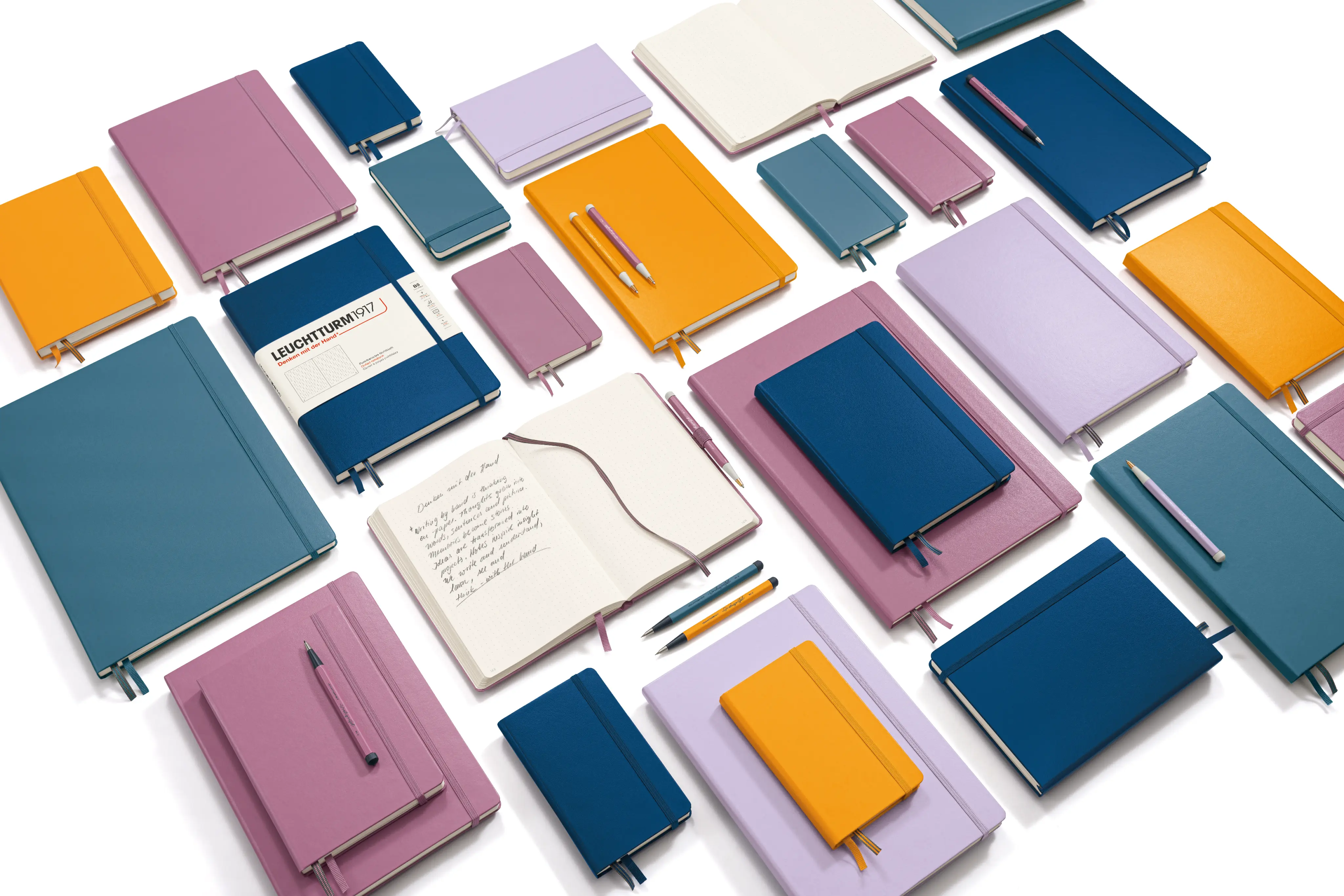 Leuchtturm1917 Notizbücher. Zahlreiche geschlossene und zwei geöffnete Notizbücher symmetrisch angeschrägt auf weißem Grund.