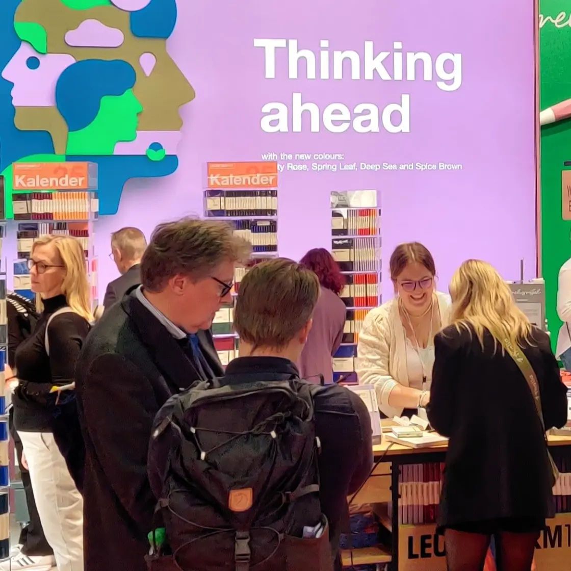 Besucherinteraktionen am Leuchtturm1917 Stand auf der Frankfurter Buchmesse 2024. Visitors and staff at a trade fair stand, shelves, text “Thinking ahead”.