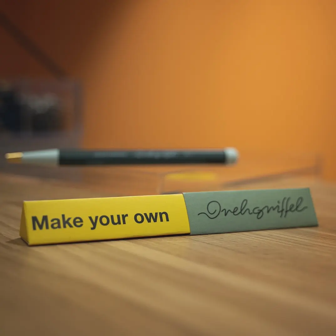 Drehgriffel Make Your Own Verpackung auf der Ambiente Messe 2024. Lettering “Make your own” and “Drehgriffel” on table, blurred Drehgriffel in the background.