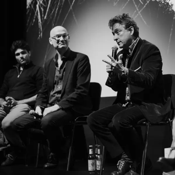 Black-and-white: panel discussion, man speaking into microphone, two people seated beside him.