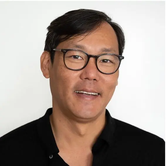 Porträtfoto – Autor des Change Journals Tim Jaudszims. Portrait of a man with black hair, glasses and a black shirt against a light background.