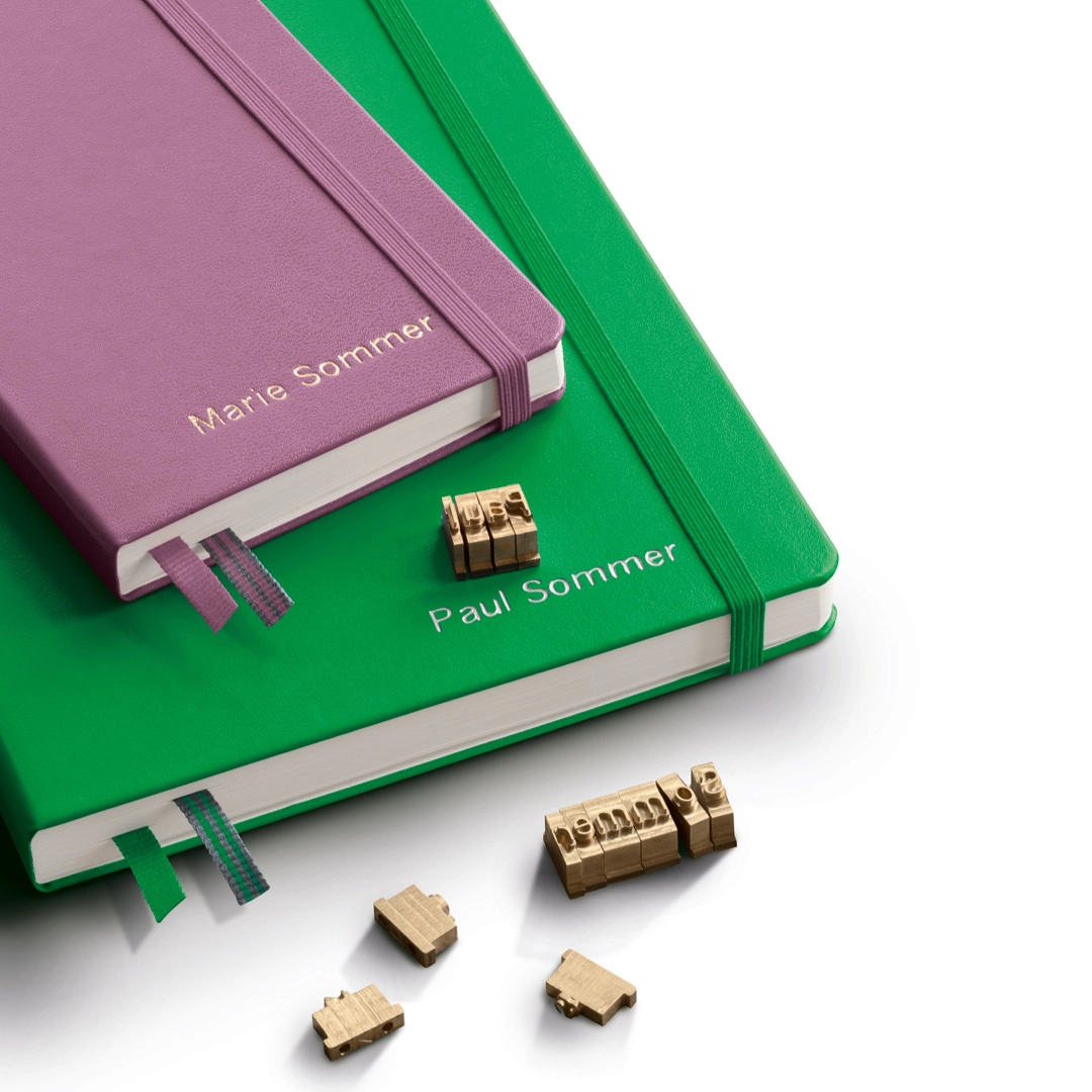 lt1917_neue_farben_2025_enp_perso Two notebooks in purple and green with elastic band, embossings “Marie Sommer” and “Paul Sommer”, metal letters.