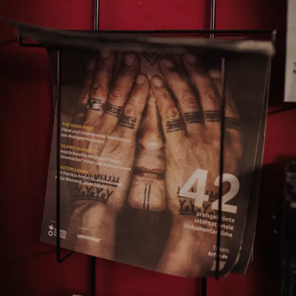 Tattooed hands cover a face on a program booklet in a wall holder.