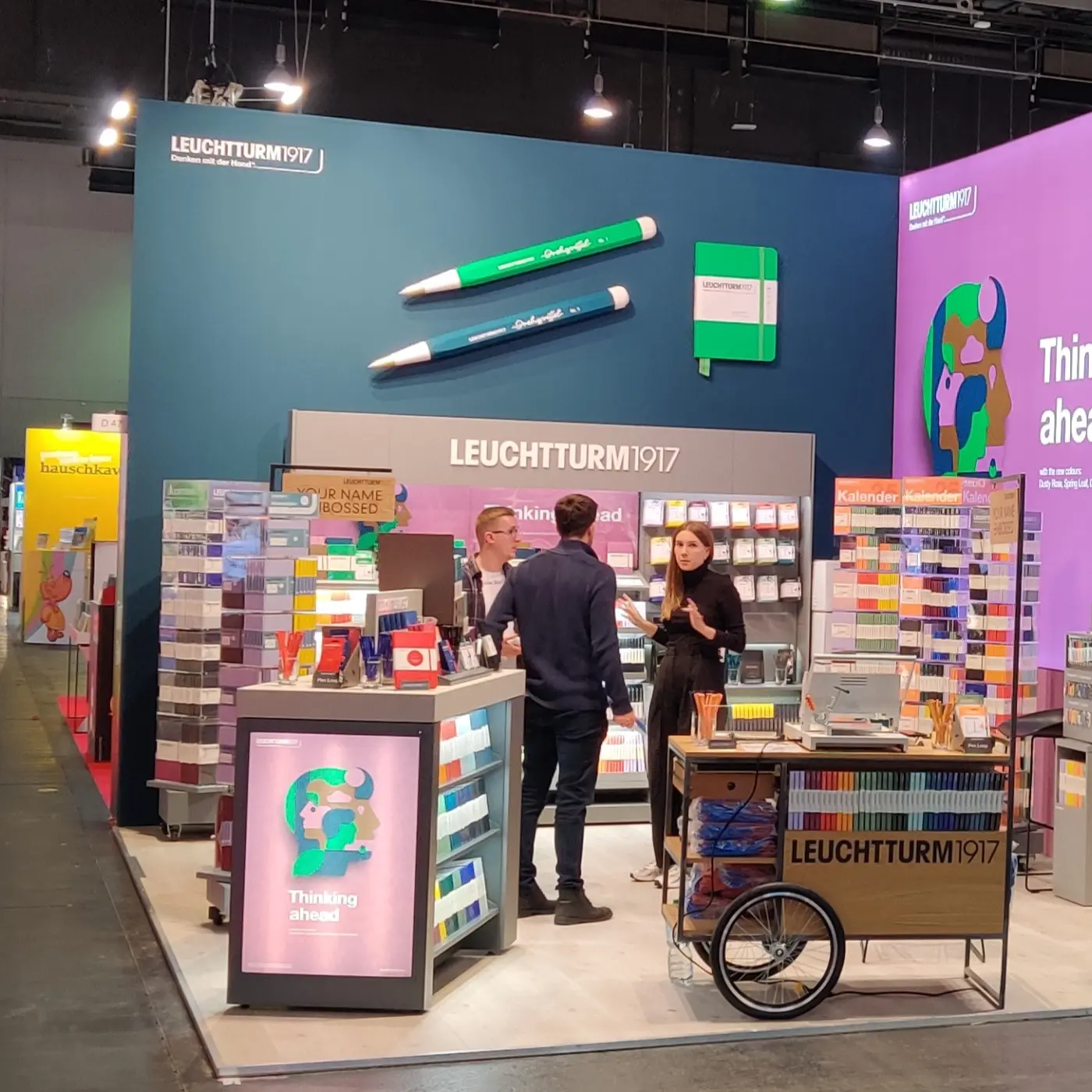 Leuchtturm1917 Messestand Frankfurter Buchmesse 2024. Trade fair stand with shelves, embossing station and three people talking.