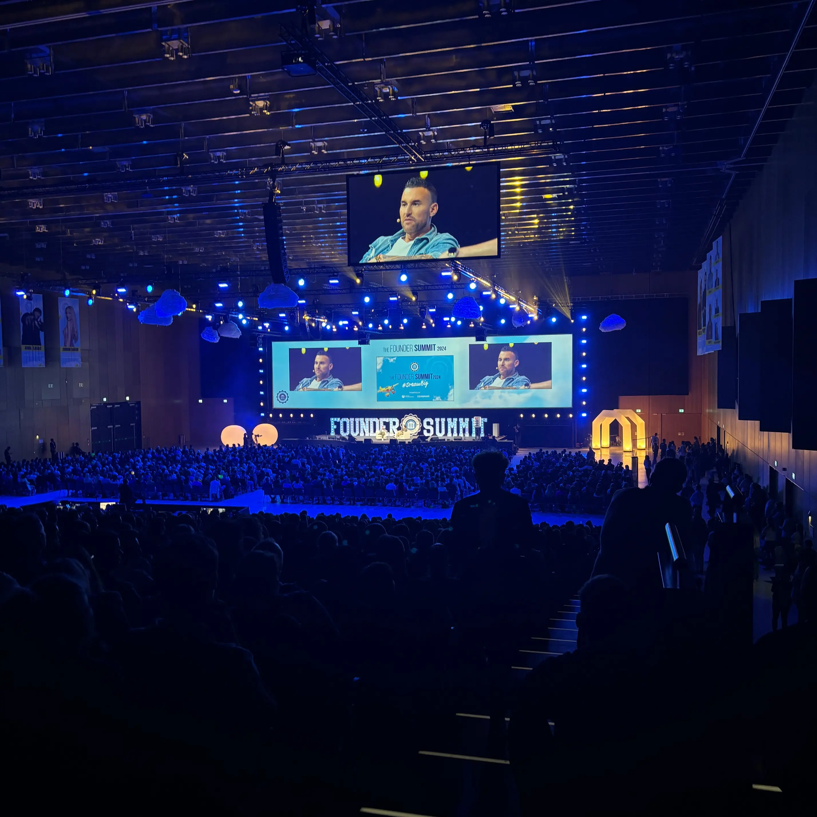 Founder Summit 2024 Bühnengespräch. Large event hall with stage, screens and audience during a talk.