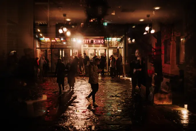 Außenaufnahme Human Rights Film Festival Berlin. Night scene outside a cinema, people in the rain, lit entrance with text “CITY KINO”.