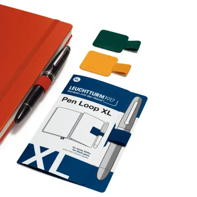 Orange notebook with attached fountain pen, Pen Loop XL packaging, and green and yellow pen holders.