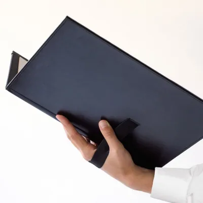 Black cover with pages, held by a hand through a hand strap.
