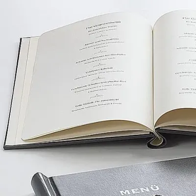 Aufgeschlagenes Buch mit gedruckten Textseiten, darunter Umschlag mit Aufdruck „MENU“.
